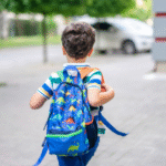 Boy with blue backpack approaches school by foot.