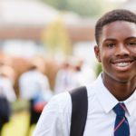 Portrait of male secondary school student in uniform outside school buildings. He is smiling to camera