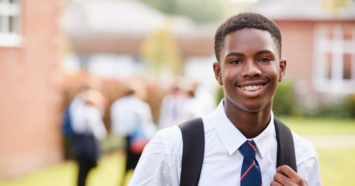 Portrait of male secondary school student in uniform outside school buildings. He is smiling to camera