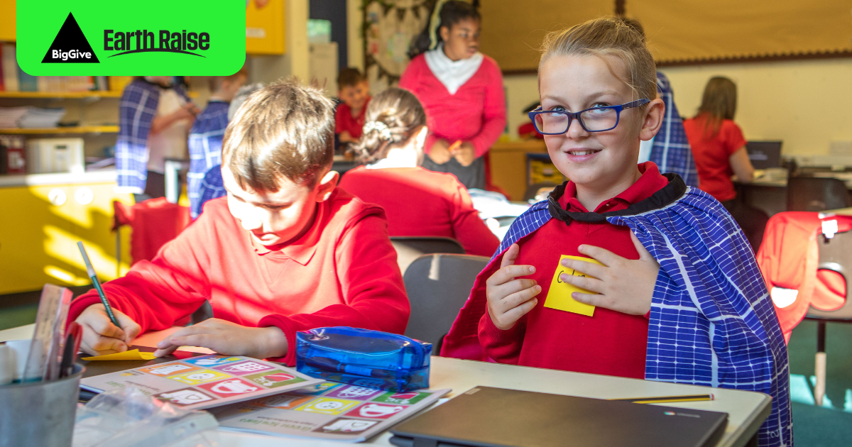 Primary school children learning about climate change. They are wearing makeshift hero capes. Overlaid is the Big Give/Earth Raise logo