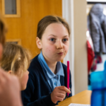 Image shows a primary school pupil holding a pen and making at thoughtful face.