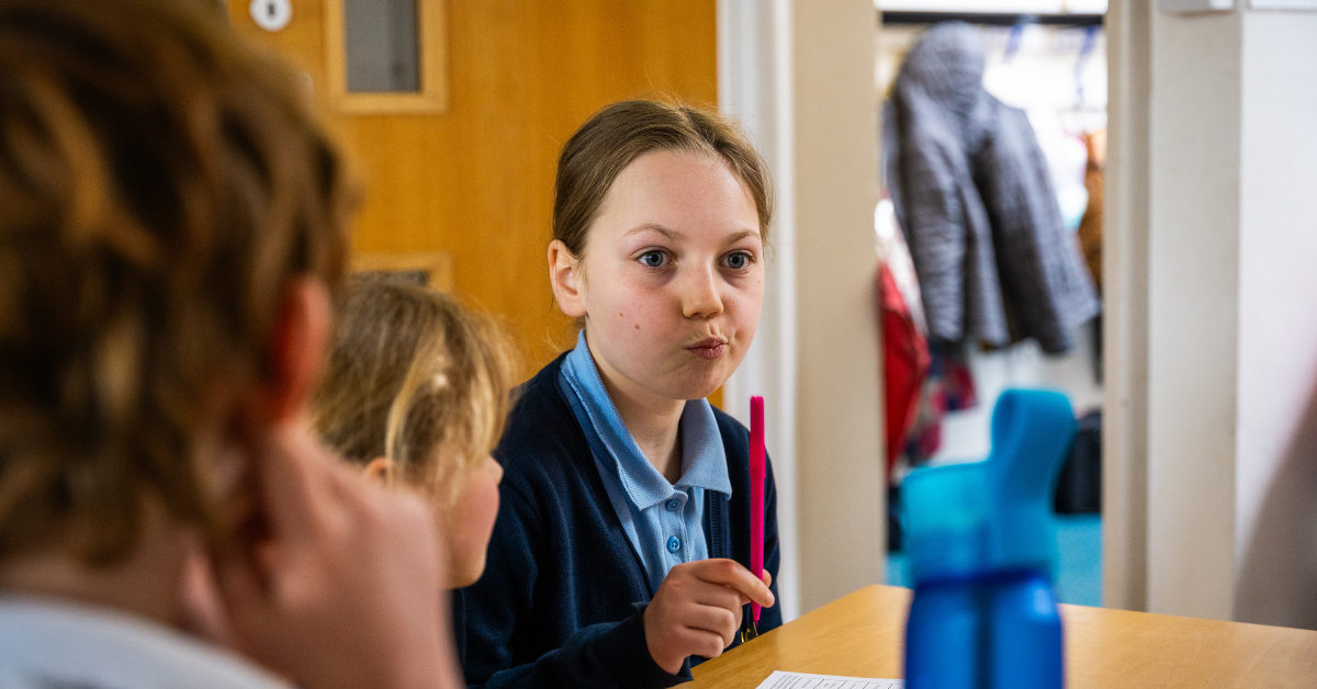 Image shows a primary school pupil holding a pen and making at thoughtful face.